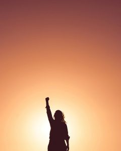 Woman standing in the sunset with her hand up to represent power and prolonging the lifespan of your car
